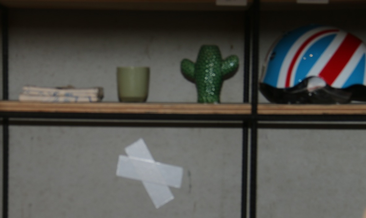 Witte absumo op grijze muur achter rek, met op de plank erboven een gekleurde fietshelm, een tas, wat handdoeken en een groene keramieken cactus.